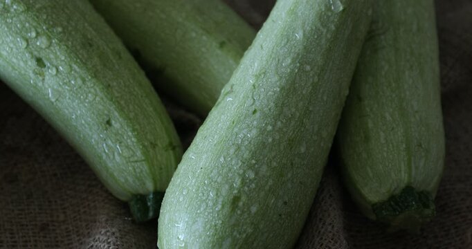 Spraying water onto fresh zucchinis at table, closeup