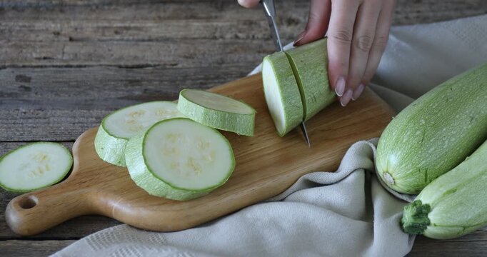 Woman cutting fresh zucchini at wooden table, closeup