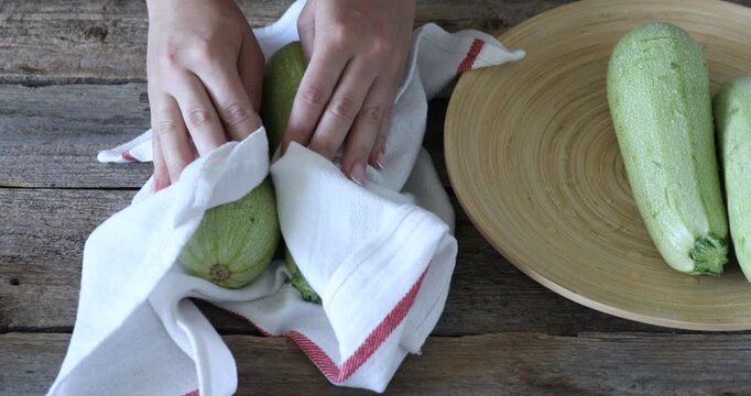 Woman wiping fresh zucchinis with towel at wooden table, closeup