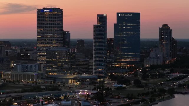 Aerial view of the Milwaukee, Wisconsin downtown skyline at dusk, showing illuminated skyscrapers along the Lake Michigan waterfront as the city lights turn
