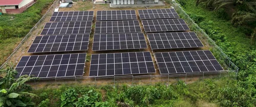 Aerial view of a solar farm with rows of photovoltaic panels installed in a fenced rural area in Tanahgrogot, Kalimantan Timur, Indonesia.
