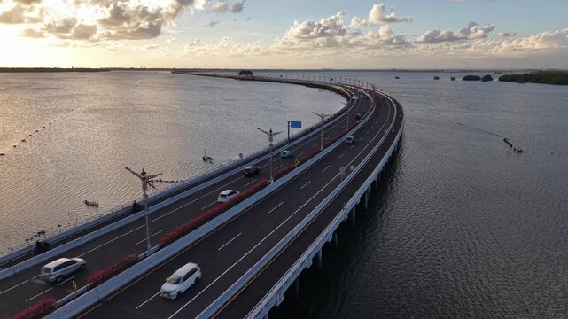 Aerial view of the Mandara Toll Road stretching over the water at sunset in Kabupaten Badung, Bali, Indonesia.