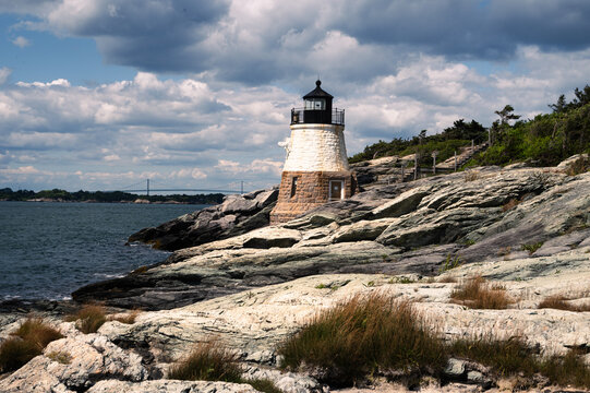 Castle Hill Lighthouse, Newport, Rhode Island, with rocky foreground, cloudy sky, Claiborne Pell bridge in background