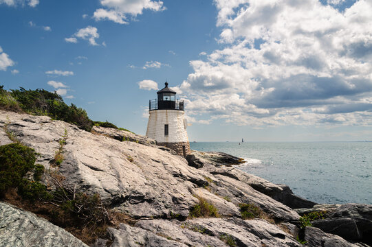 Castle Hill Lighthouse, Newport, Rhode Island, rocky foreground, cloudy sky, sailboats in background