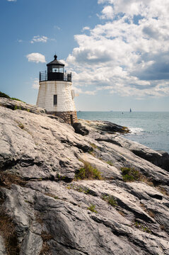 Castle Hill Lighthouse, Newport, Rhode Island, with rocky foreground and cloudy sky, sailboats in background