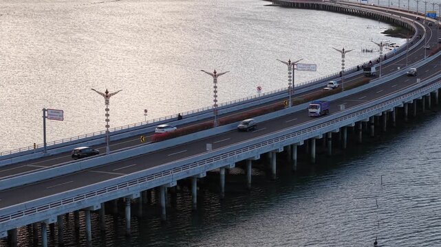 Aerial view of Mandara Toll Road with vehicles driving over the water in Kabupaten Badung, Bali, Indonesia.