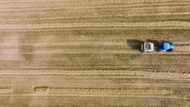 Baled tractor towing round bale golden field aerial view