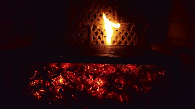 Watch fire burning in a grill with glowing coals and flames at night during a gathering in a backyard setting