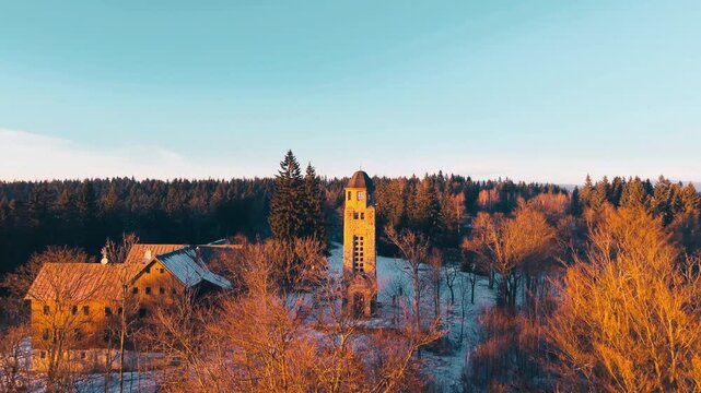 Aerial view of Bramberk lookout tower surrounded by autumn-colored trees and light snow in the forest in Lucany nad Nisou, Liberec Region, Czechia.
