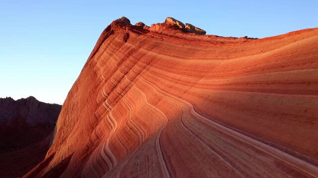 Panoramic sandstone ridge with sweeping curved striations lit by warm low-angle sunlight, showing layered red and ochre bands, rugged texture, deep scale, and dramatic desert perspective
