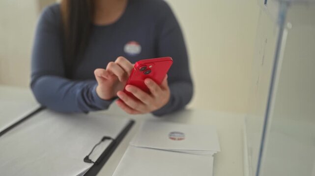 Woman finger tapping red smartphone at a polling station inside a community building; civic duty pride.