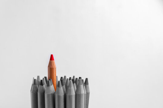 Red pencil standing out from crowd of gray pencils with white copy space, real photography, not AI generated.
