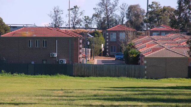Suburban brick townhouses with terracotta tiled roofs bordering an open grassy reserve&nbsp;and nearby highway infrastructure in Melton, Melbourne, Australia.&nbsp;Residential housing in an outer suburb