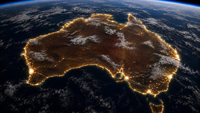Australia at Night &ndash; Orbital view of Australia outlined by coastal city lights beneath scattered clouds and a curved horizon.