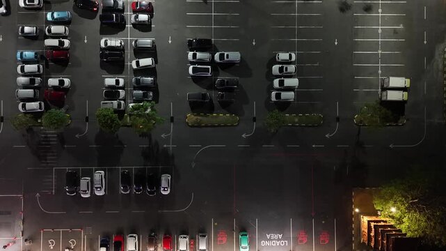 Aerial view of Lotte Mart parking lot at night with parked cars and illuminated loading area in Kecamatan Denpasar Selatan, Bali, Indonesia.
