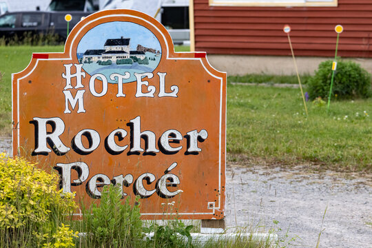Gaspesie, Quebec, 15 July 2026 : Weathered orange sign for Hotel Rocher Perce stands in a grassy area with a building in the background.