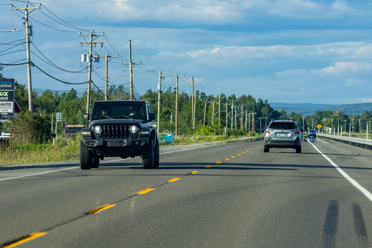 Gaspesie, Quebec, 11 July 2026 : A black Jeep Wrangler drives on a multi-lane highway with power lines and trees under a blue sky.