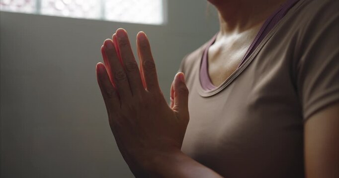Close up of Asian Woman Hands in Sportswear Praying in Yoga Pose, Faceless Female Practicing Namaste Mudra in Cozy Room with Soft Morning Sunlight, Mental Wellness Lifestyle.
