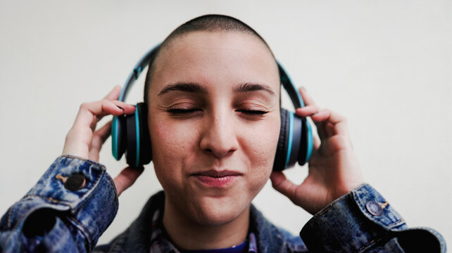 Alternative young woman with shaved head listening to music on wireless headphones - Natural beauty and self expression concept
