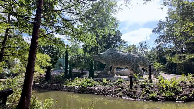 A beautiful panning shot revealing the magnificent restored Crystal Palace Dinosaurs in their natural park setting.