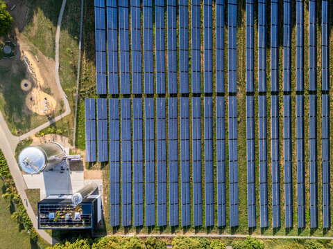 Aerial view of a solar farm with rows of photovoltaic panels and a solar thermal facility featuring large storage tanks in Germany.