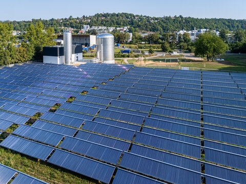 Aerial view of a large solar thermal collector field with industrial storage tanks and green surroundings in Germany.