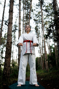 Young karate student with red belt practicing a strong stance and focused discipline during an outdoor forest training session for martial arts practice