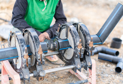 A technician using an angle grinder to prep black HDPE pipes secured in a butt fusion welding machine on a job site.