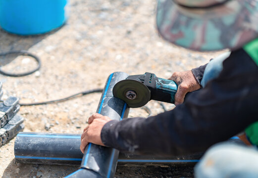 Laborer using an electric grinding tool to cut and shape high-density polyethylene piping during utility installation.