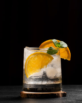 Refreshing Citrus Cocktail With Orange Garnish Ice and Mint on Black Wooden Table