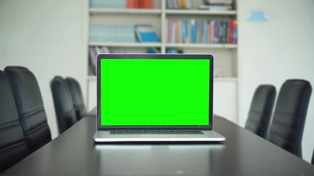 Green screen laptop on a table in a meeting room with chairs and bookshelves