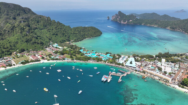 Aerial view of Koh Phi Phi featuring turquoise bay waters, numerous boats, a bustling pier, and lush green hills in Khlong Phon, Krabi, Thailand.