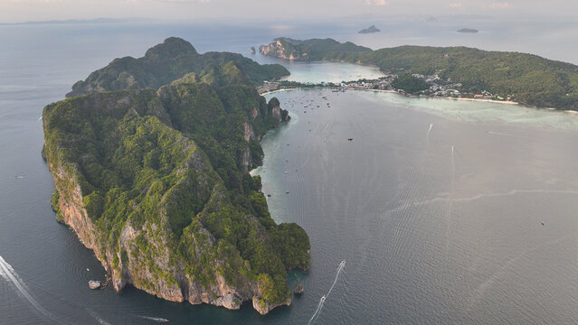 Aerial view of Koh Phi Phi featuring lush green cliffs, turquoise waters, and boats anchored near the sandy beach in Khlong Phon, Krabi, Thailand.