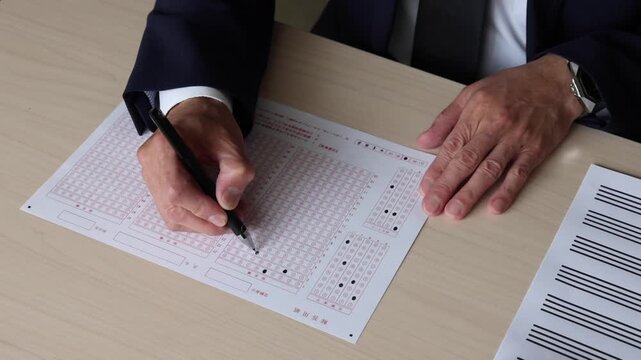 マークシート方式の解答用紙にペンで回答を記入する手元