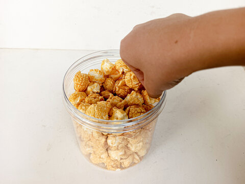 A hand taking popcorn from a jar. White background.
