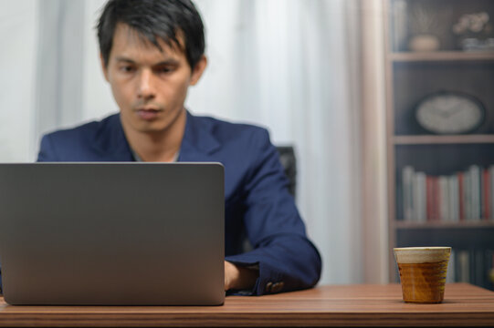 Modern young man working on laptop at home with coffee and bookshelf in background