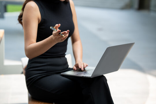 Cropped woman in black dress using laptop and holding pen during an online meeting or work discussion in a modern office setting.