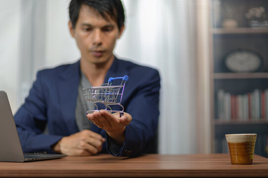 Man in formal suit examining miniature shopping cart in modern office setting