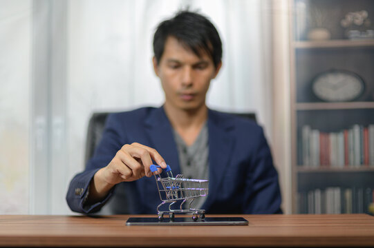 Young man in formal jacket with dark hair examining a miniature shopping cart on a table