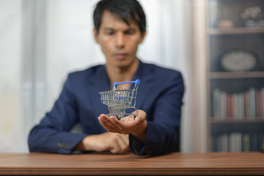 Man Holding Small Shopping Cart Model at Wooden Table in Indoor Setting