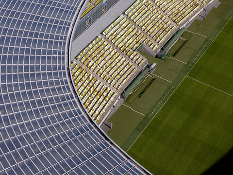 Aerial view of the Polsat Plus Arena Gdansk stadium, highlighting the curved glass roof structure and rows of yellow and white seats overlooking the green pitch in Gdansk, Poland.