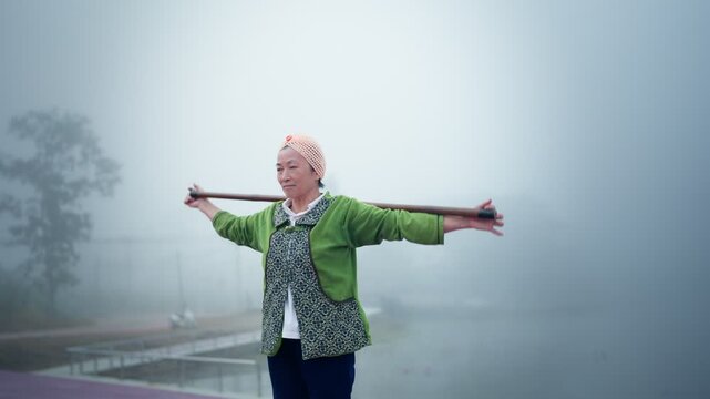 Senior Asian woman practicing tai chi in foggy outdoor nature during morning routine, active senior lifestyle and wellness concept