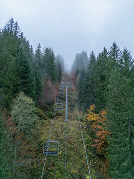 Aerial view of a ski lift ascending through a dense forest with autumn foliage and misty conditions in La Giettaz, Auvergne-Rhone-Alpes, France.