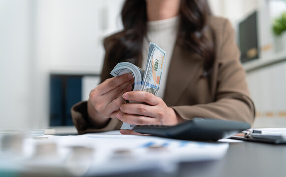 Businesswoman counting cash while reviewing financial records for budgeting, payroll, and money management.