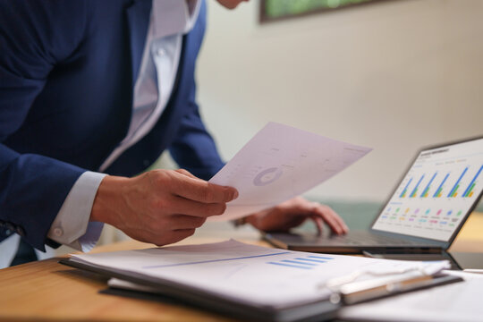 Businessman reviewing financial documents with laptop for audit, compliance, and business analysis, highlighting accurate reporting and decision making.