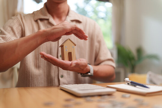 Man protects a model house with his hands, representing home insurance, property security, mortgage planning, and financial protection for homeowners and long-term asset stability.
