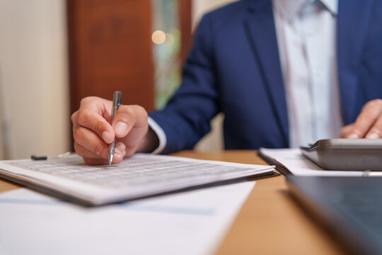 Businessman reviewing accounting records and writing financial data with calculator, supporting accurate bookkeeping and business reporting.