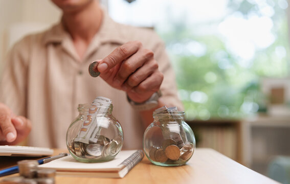 Man saving cash and coins in glass jars for budgeting, emergency funds, and future financial goals, representing disciplined money management and long-term planning.