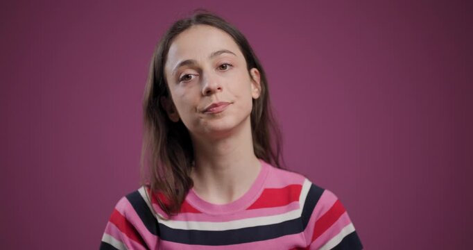 Young woman ponders deeply, dressed in striped shirt against pink background