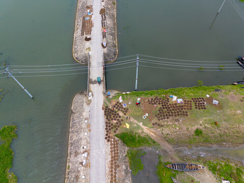 Aerial view of circular cow dung cakes drying on the ground near a rural road and water in Kishoreganj, Dhaka Division, Bangladesh.